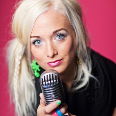 Amelie Nörgaard håller i en mikrofon mot en rosa bakgrund.
