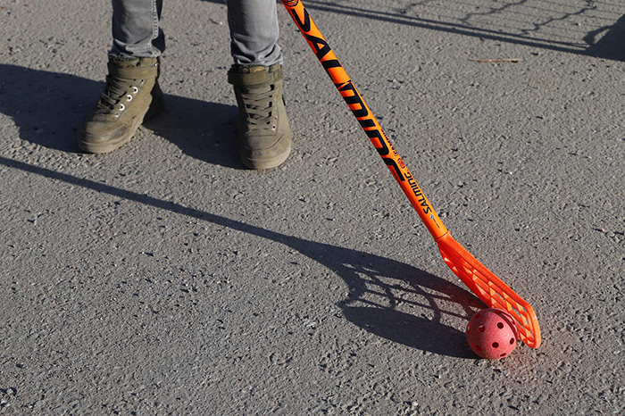En person utomhus håller i en innebandyklubba med tillhörande boll.